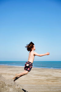 Woman jumping on beach against clear sky