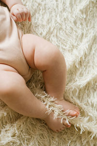 Belly and legs of a newborn baby in a bodysuit lying on a light bed, top view