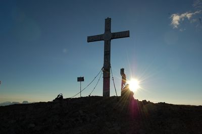 Low angle view of cross on land against sky during sunset