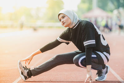 Thoughtful female athlete stretching on track