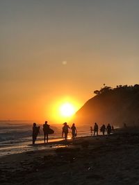 People enjoying at beach against sky during sunset