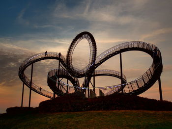 Low angle view of rollercoaster against sky at sunset