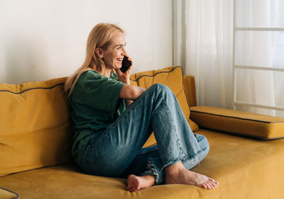 Attractive middle aged woman chatting cheerfully on the phone while sitting on the couch. person