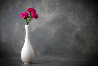 Close-up of rose flower in vase on table against wall