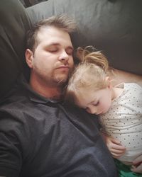 High angle view of father with daughter sleeping on sofa