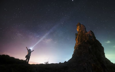 Low angle view of man with flashlight standing by rock formation against sky