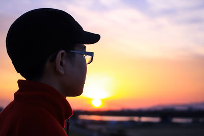 Side view of boy wearing eyeglasses standing against cloudy sky during sunset