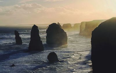 Rocks in sea against sky during sunset