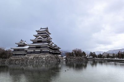 Traditional building at lake against cloudy sky