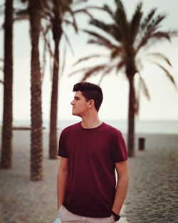 Young man looking away while standing at beach