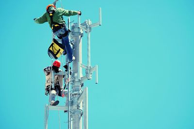 Low angle view of technicians repairing electric pole against clear blue sky