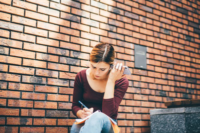 Young woman standing against brick wall