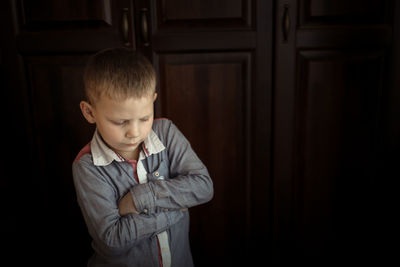 Boy is serious and offended, the concept of children's emotions, brown background in real interior