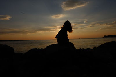 Silhouette woman sitting on beach against sky during sunset