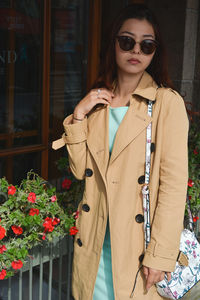 Young woman wearing sunglasses standing against red wall