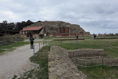 People on field by historic building against sky