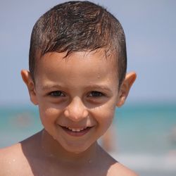 Close-up portrait of wet boy smiling while standing at beach