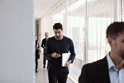 Businessman using smart phone while walking with colleagues in corridor during leaving office