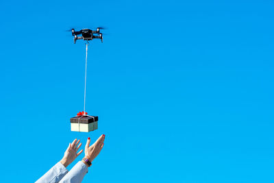 Low angle view of person holding gift on drone against blue sky