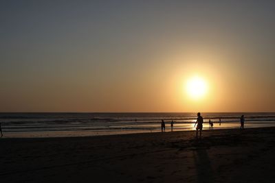 Silhouette people on beach against sky during sunset