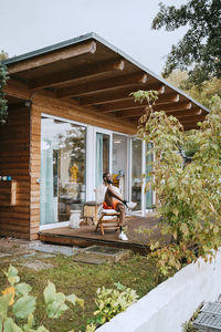 Smiling mature man sitting on chair on porch outside tiny house