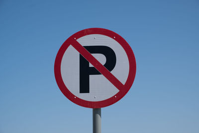 Low angle view of road sign against clear blue sky