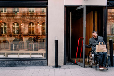 Disabled mature man with shopping bag leaving store in city