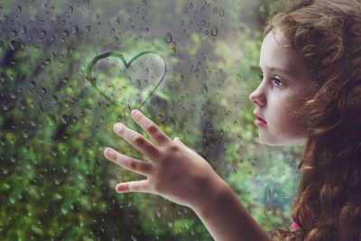 Sad curly little girl looking out the rain drop window and draw heart. toning for instagram filter.