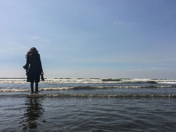 Rear view of woman standing on beach against sky