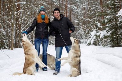 Young man and woman playing with siberian huskies on snowy field