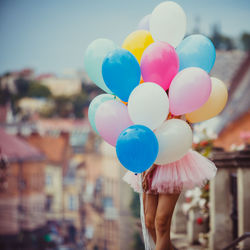Low section of person holding balloons against sky