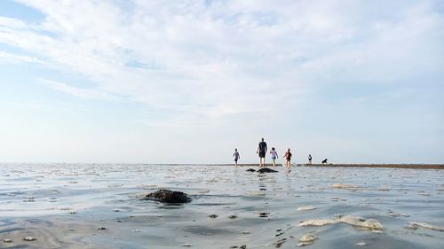 Rear view of people walking at beach against sky