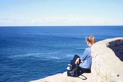 Young woman sitting by sea against sky