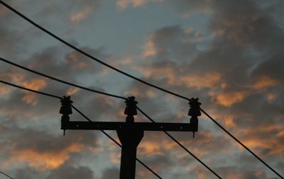 Low angle view of silhouette electric cable tower against sky