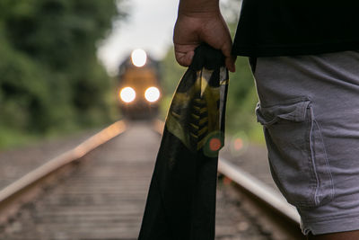 Midsection of person holding fabric while standing on railroad track