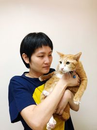 Portrait of happy young woman holding cat against white background