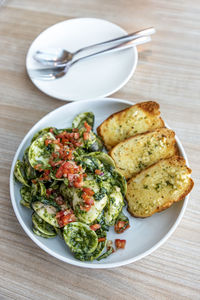 Clam pesto salsa in a round white plate, next to an empty plate and cutlery, on a wood grain table.