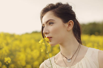 Close-up of thoughtful young woman with yellow flowers at farm