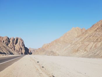 Scenic view of desert road against clear blue sky