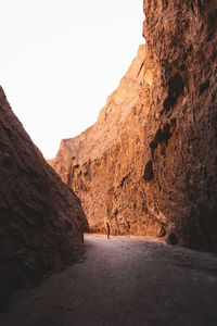 Person walking on rock formation against clear sky