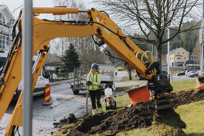 Female road worker and excavator at digging site