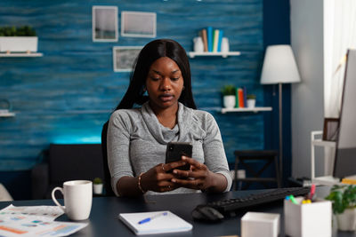 Portrait of young woman using mobile phone while sitting in cafe