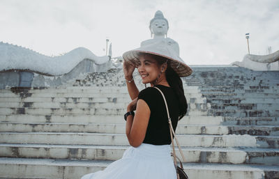 Smiling woman standing by staircase against sky