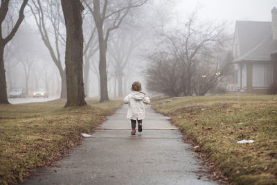 Rear view of girl wearing raincoat while walking on footpath during foggy weather