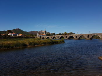 Arch bridge over river against clear blue sky