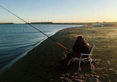 Rear view of man fishing in sea against sky