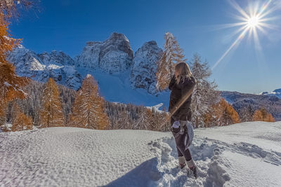 Blonde woman looking at a dolomite mountain and orange colored larch forest on a beautiful sunny day