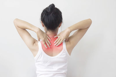 Rear view of woman with shoulder pain standing against white background