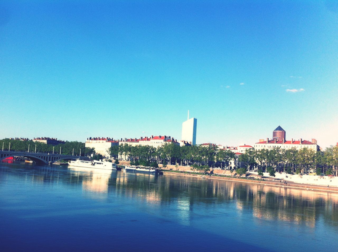 water, waterfront, blue, clear sky, building exterior, architecture, built structure, copy space, reflection, lake, sky, nautical vessel, transportation, river, nature, tranquility, mode of transport, outdoors, sea, tree