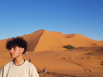 Young man standing at desert against clear sky